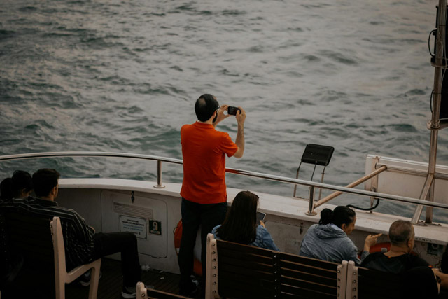 Waiting whale watcher with his smart phone, standing at the stern of a tour boat.