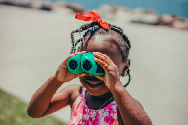 Little girl with binoculars whale watching from land.