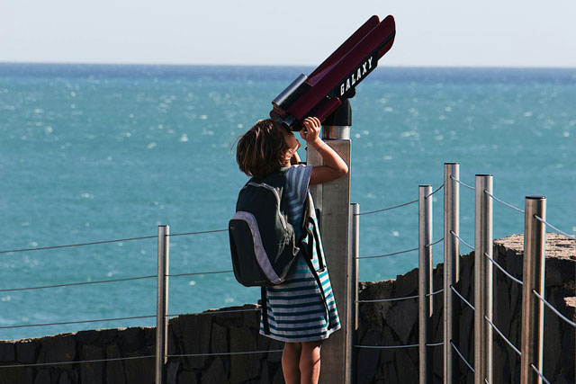 Young girl trying to use mounted binoculars for whale watching from land.